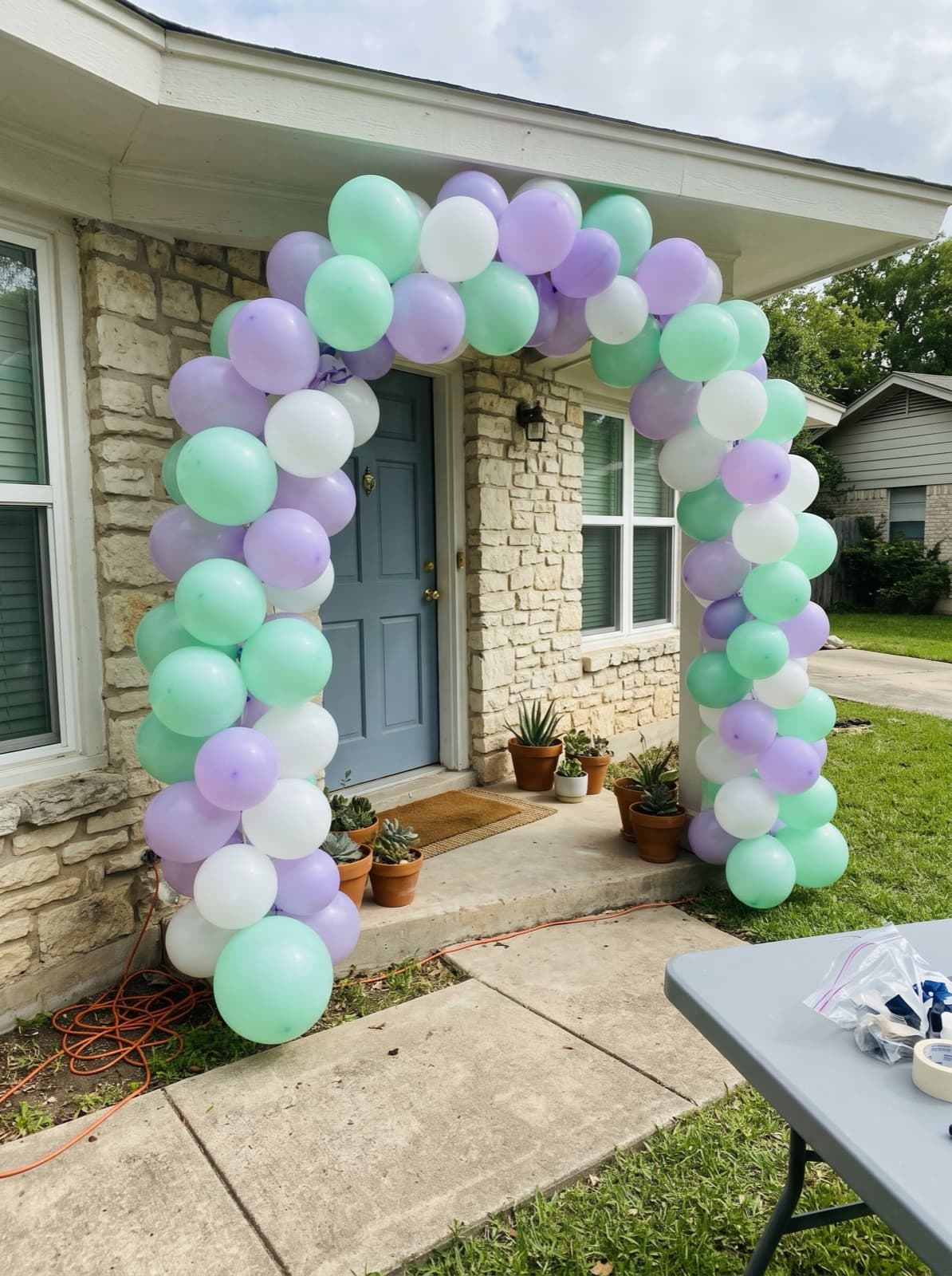 Balloon arch in mint, lilac and white over the front door of a limestone house