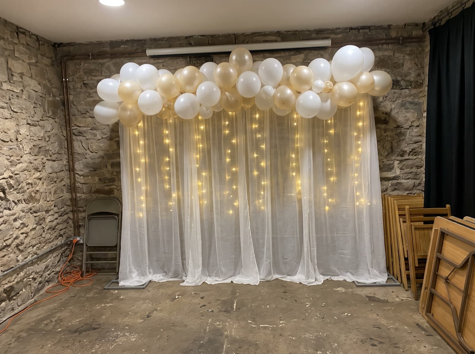 Draped backdrop with balloons and lights in a stone-walled hall