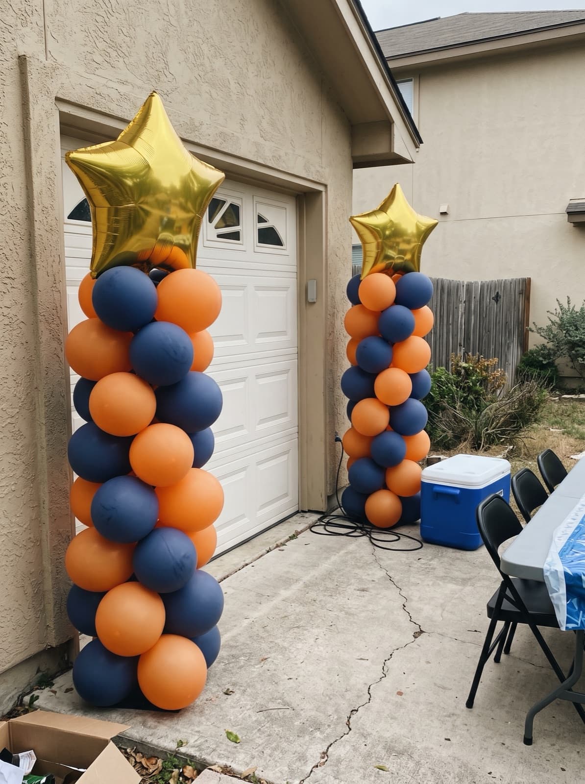 Pair of spiral balloon columns in orange and navy with gold star toppers at a San Antonio graduation party