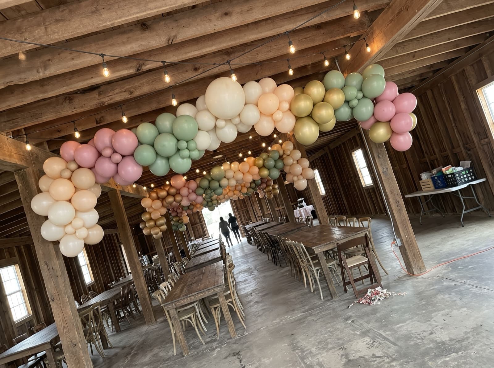 Hanging balloon garland canopy over farm tables in a barn venue